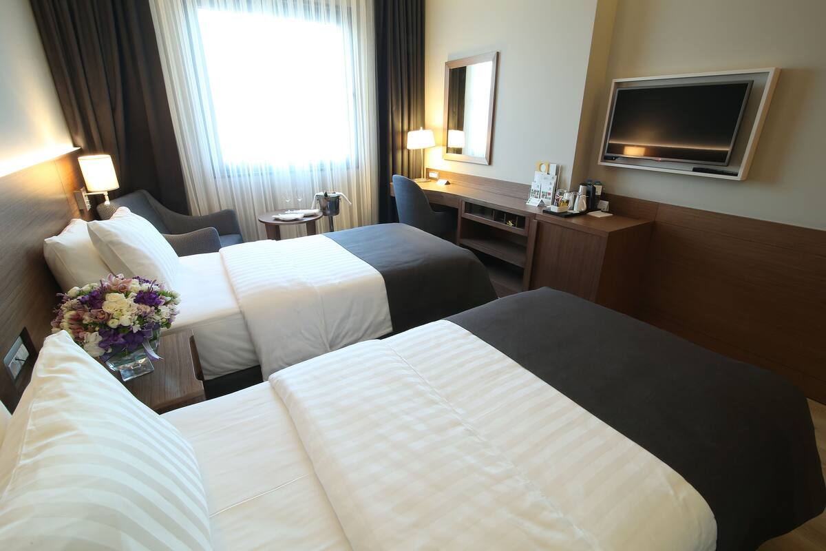 Ein Hotelzimmer mit zwei Betten, einem Schreibtisch, einem Stuhl, einem Fernseher und einem Fenster mit Vorhängen.