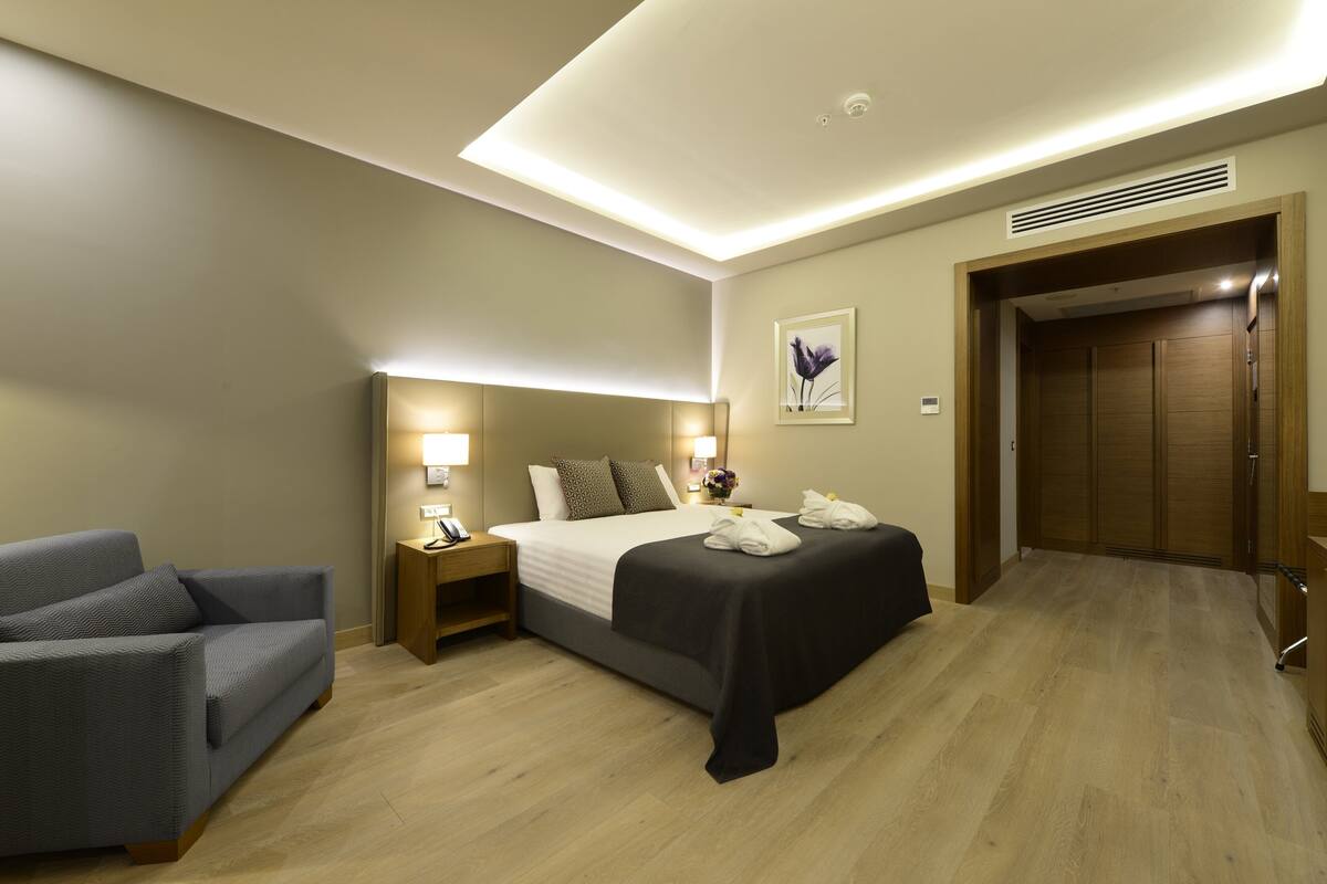 Ein Hotelzimmer mit einem Bett, einem Nachttisch, einem Sessel und einem Holzschrank.
