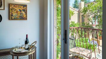 A room with a dining table, a wine bottle, and a chair. There is a window with a view of greenery and buildings outside.