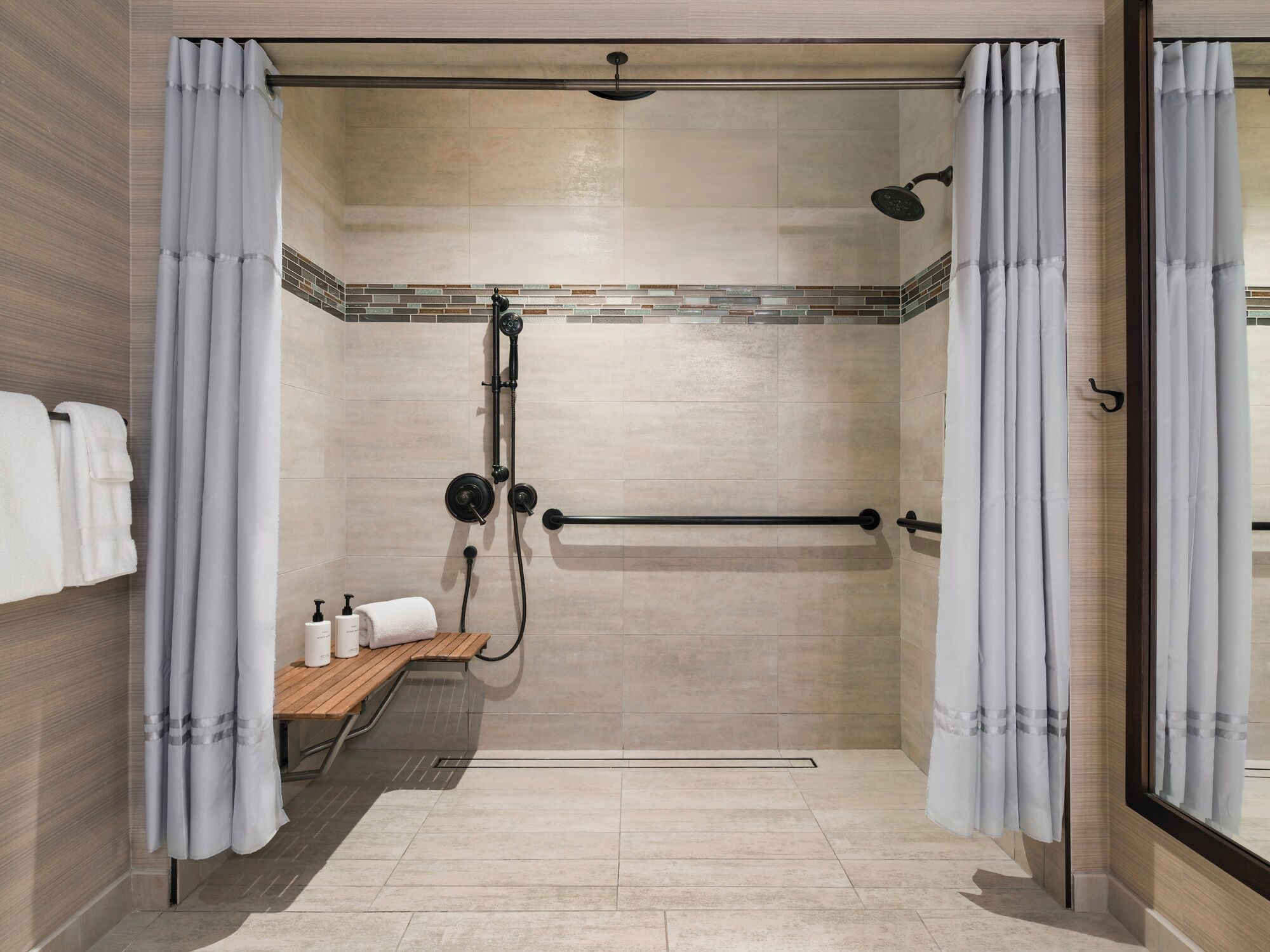 A shower area with a glass-enclosed shower, a wooden bench, and a towel rack.