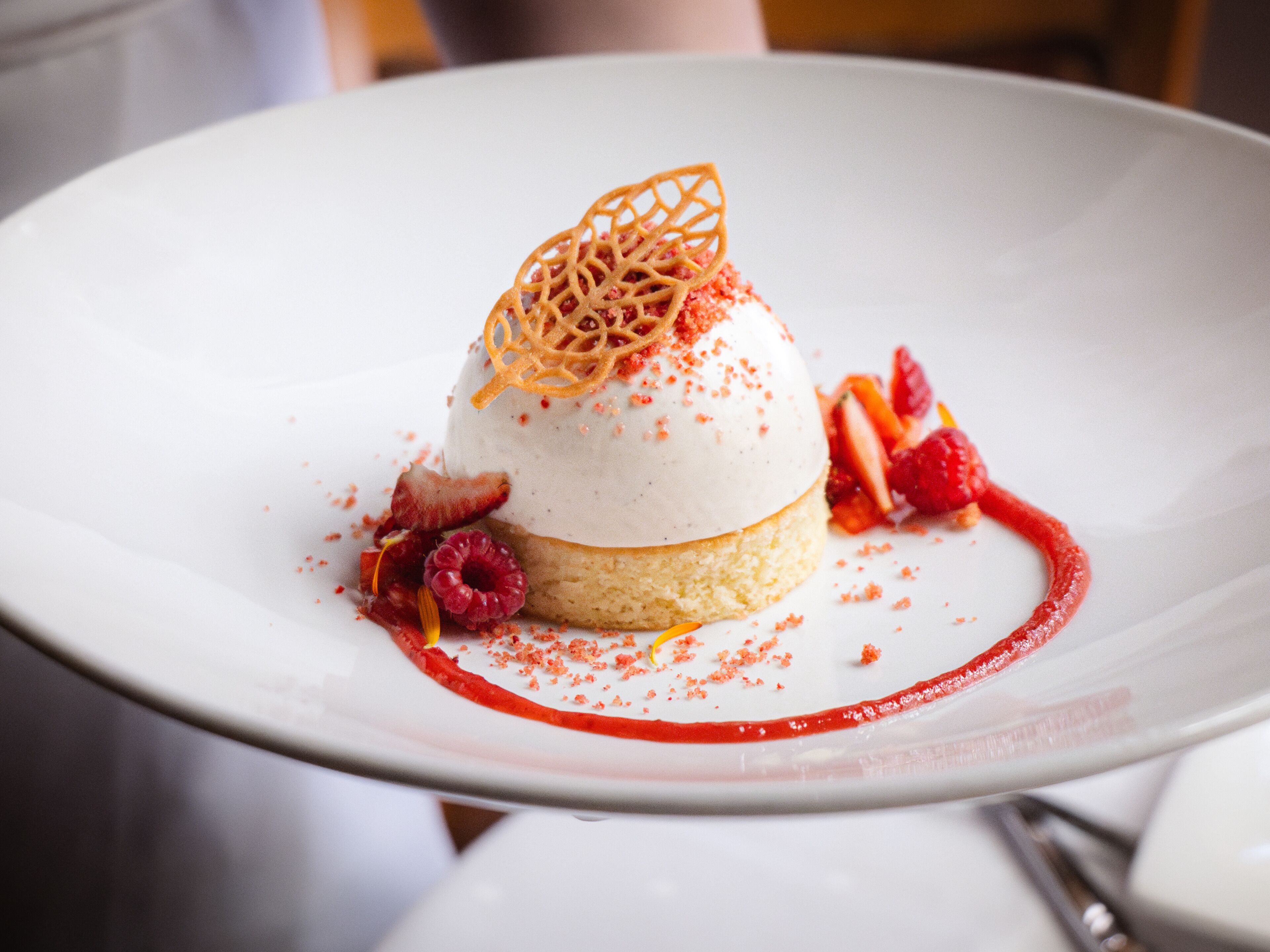A dessert on a white plate with a lattice topping, strawberries, raspberries, and a red sauce.