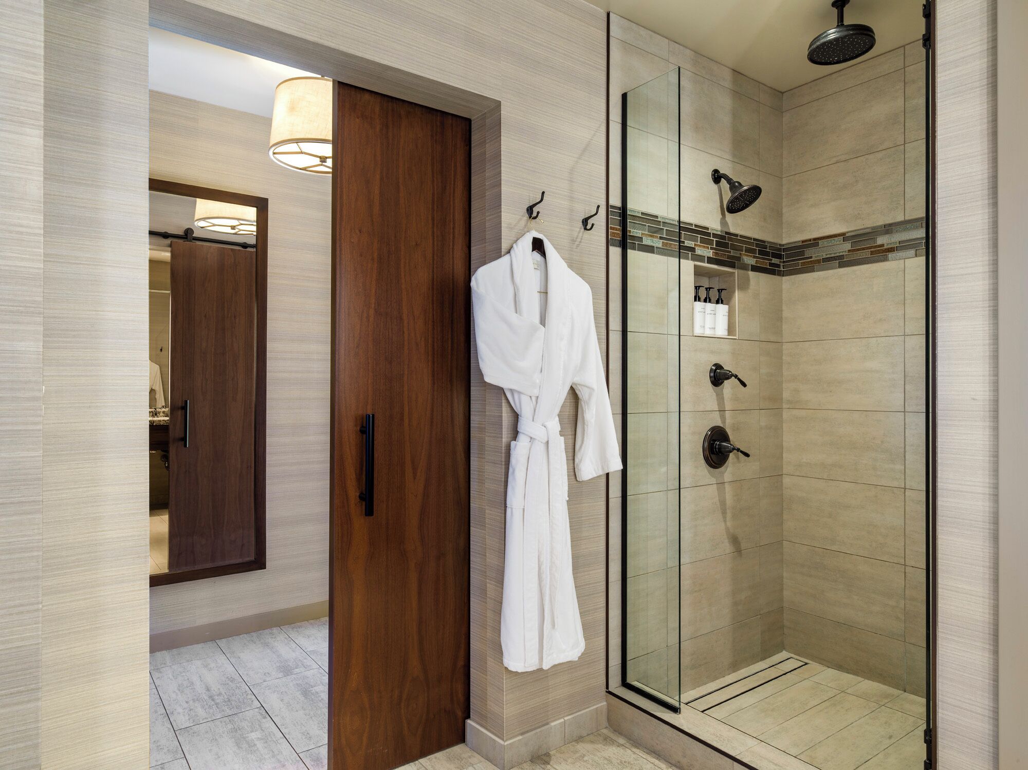 Un baño moderno con cabina de ducha de vidrio, puerta de madera y una bata colgada en un perchero.