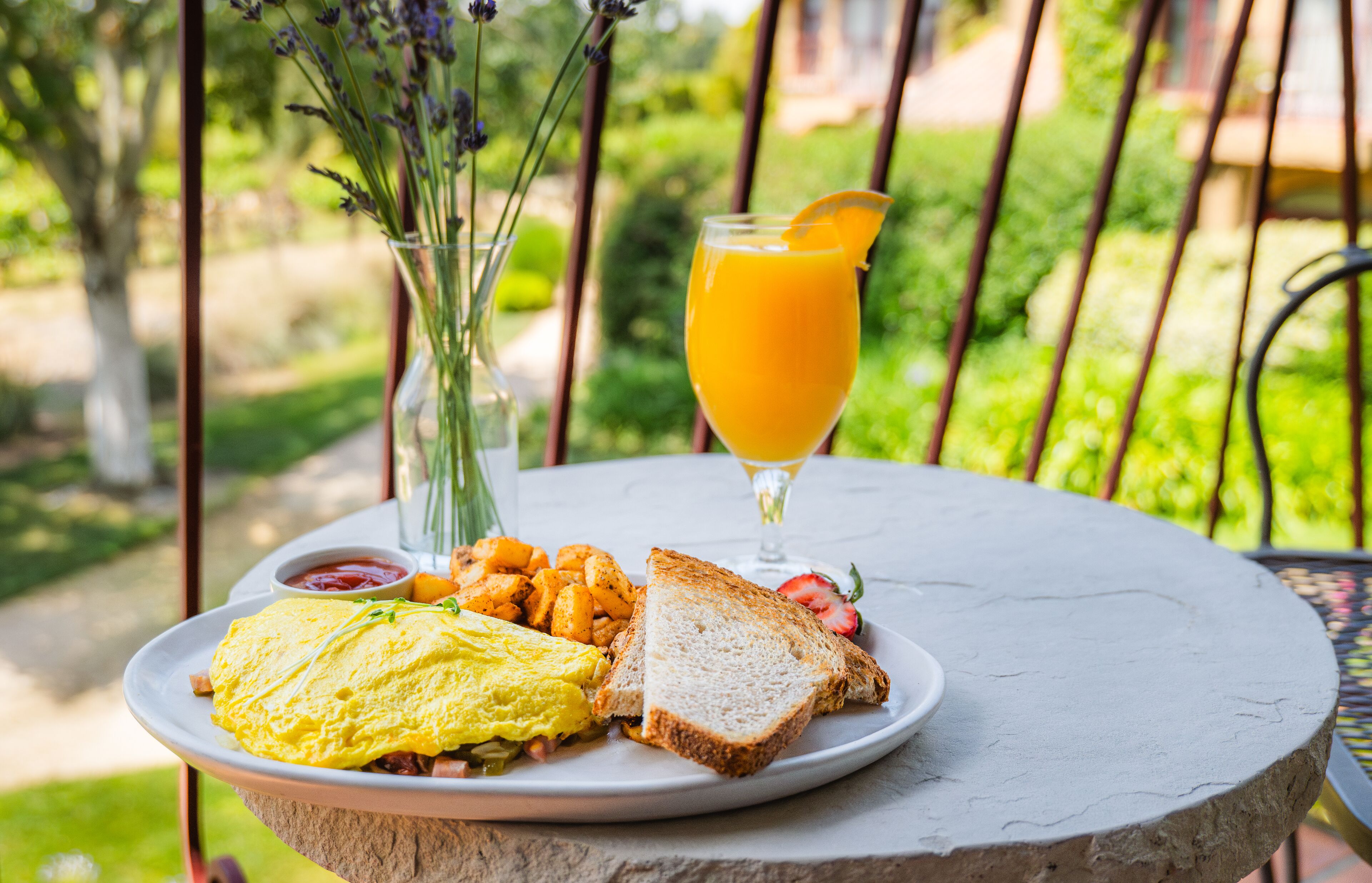 A breakfast plate with eggs, toast, and orange juice on a stone table outdoors.