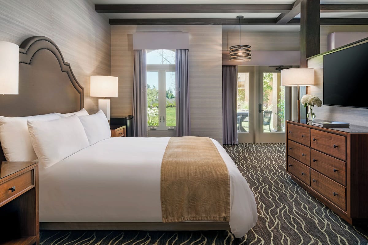A hotel room with a large bed, a TV, a dresser, and a view of the outdoors.