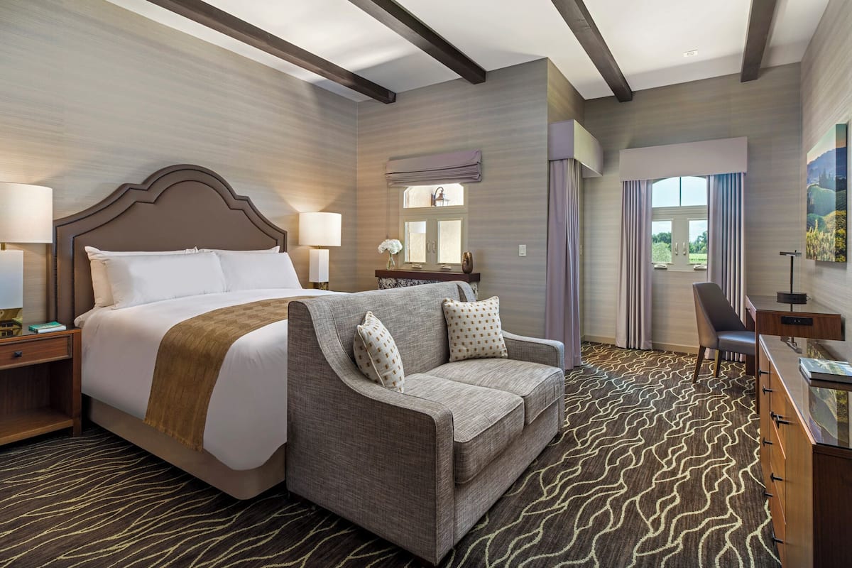 A hotel room with a large bed, a sofa, a desk, and a view of the outdoors.