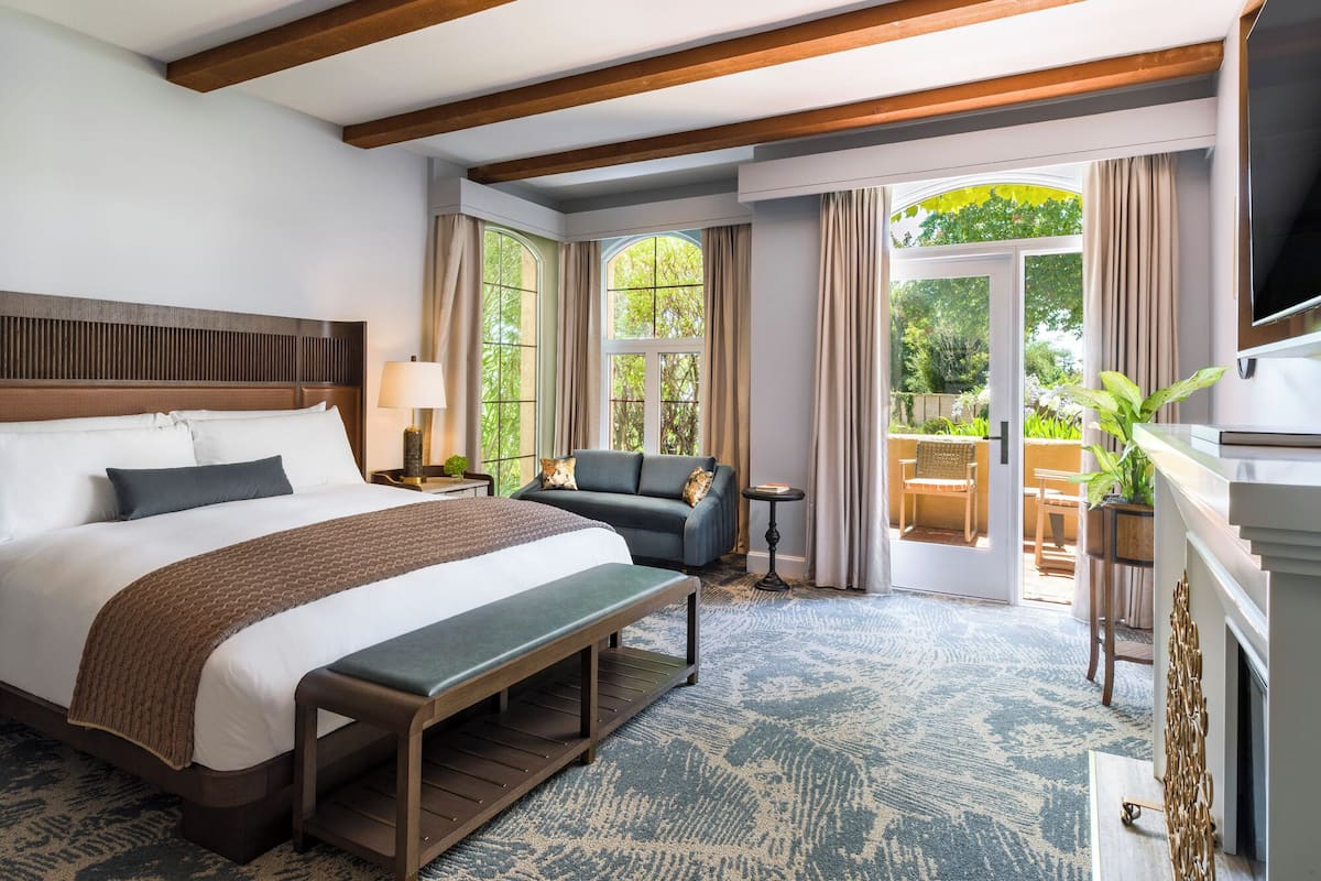 A hotel room with a large bed, a bench, a sofa, a TV, and a fireplace.