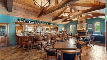 A rustic bar area with wooden furniture, a long counter with wine bottles, and a fireplace.