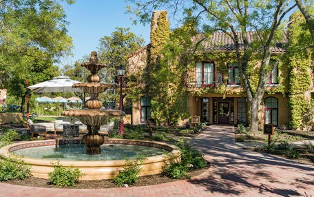 A fountain surrounded by a brick pathway, with a building featuring a tiled roof and ivy-covered walls in the background.