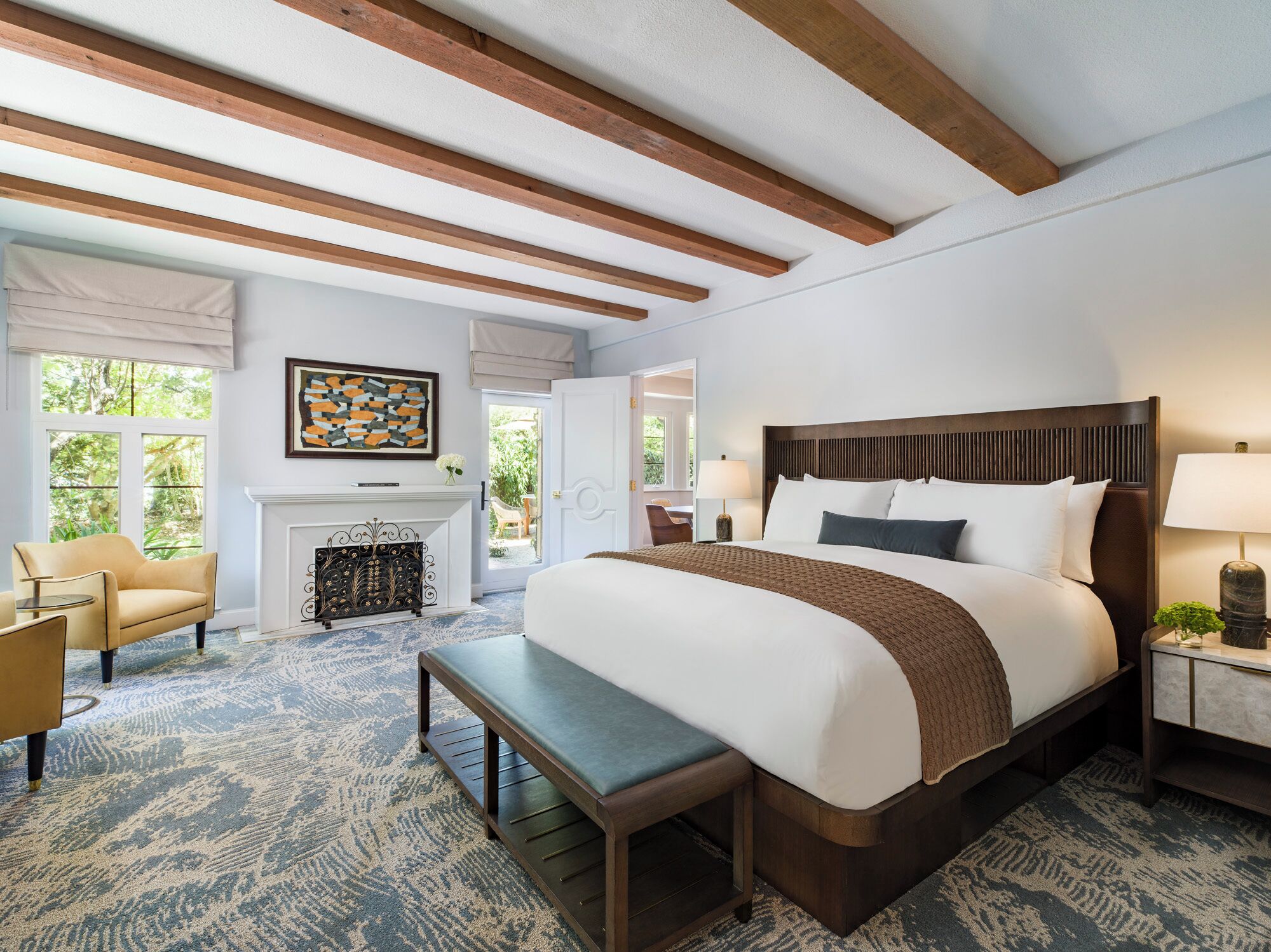 A spacious bedroom with a large bed, a bench, a fireplace, and a view of the outdoors.