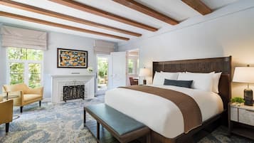 A spacious bedroom with a large bed, a bench, a fireplace, and a view of the outdoors.