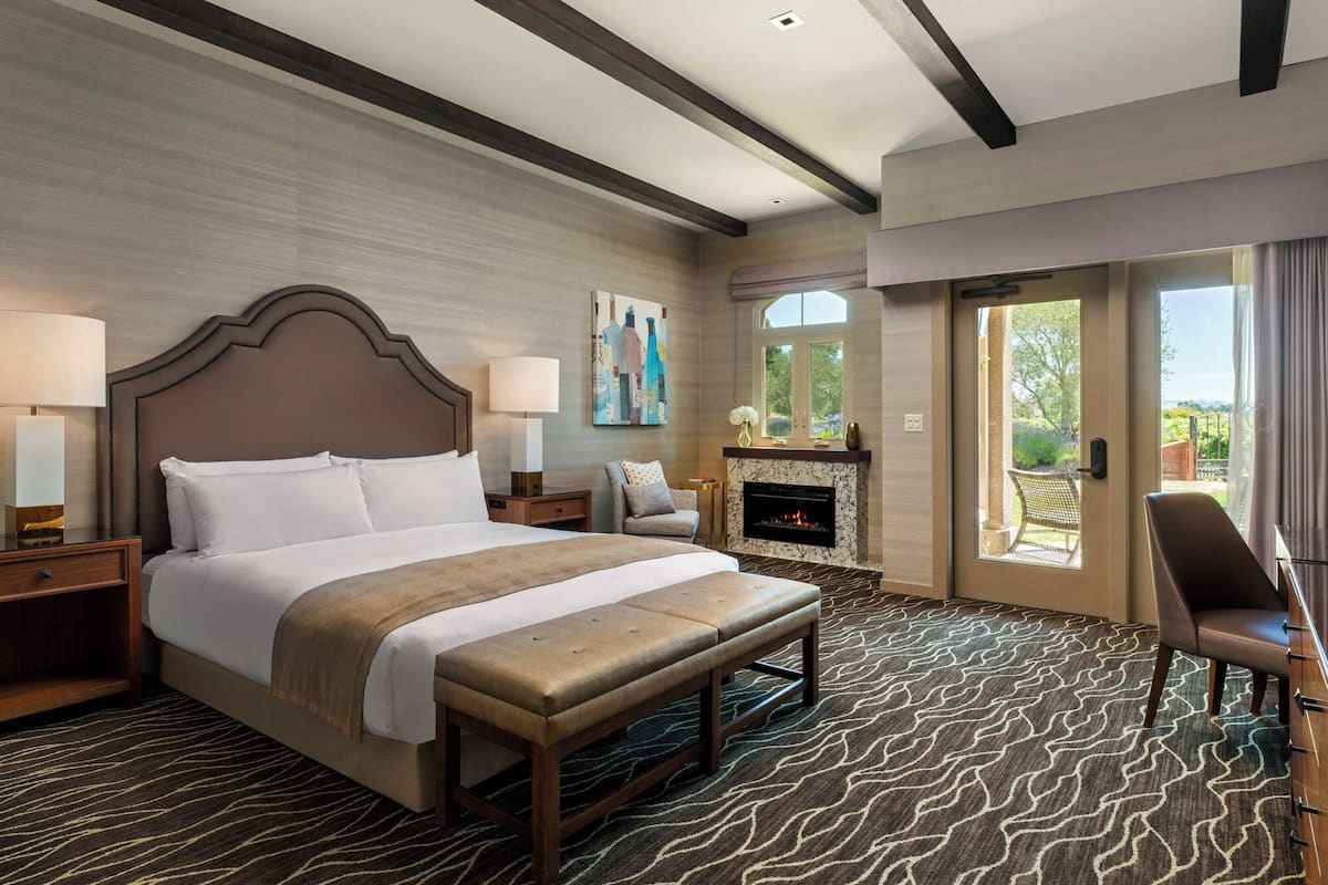 A hotel room with a large bed, a fireplace, a bench, and a view of the outdoors.