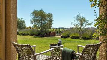 Un patio con dos sillas de mimbre y una mesita, con vistas a un área verde con una pérgola y árboles.