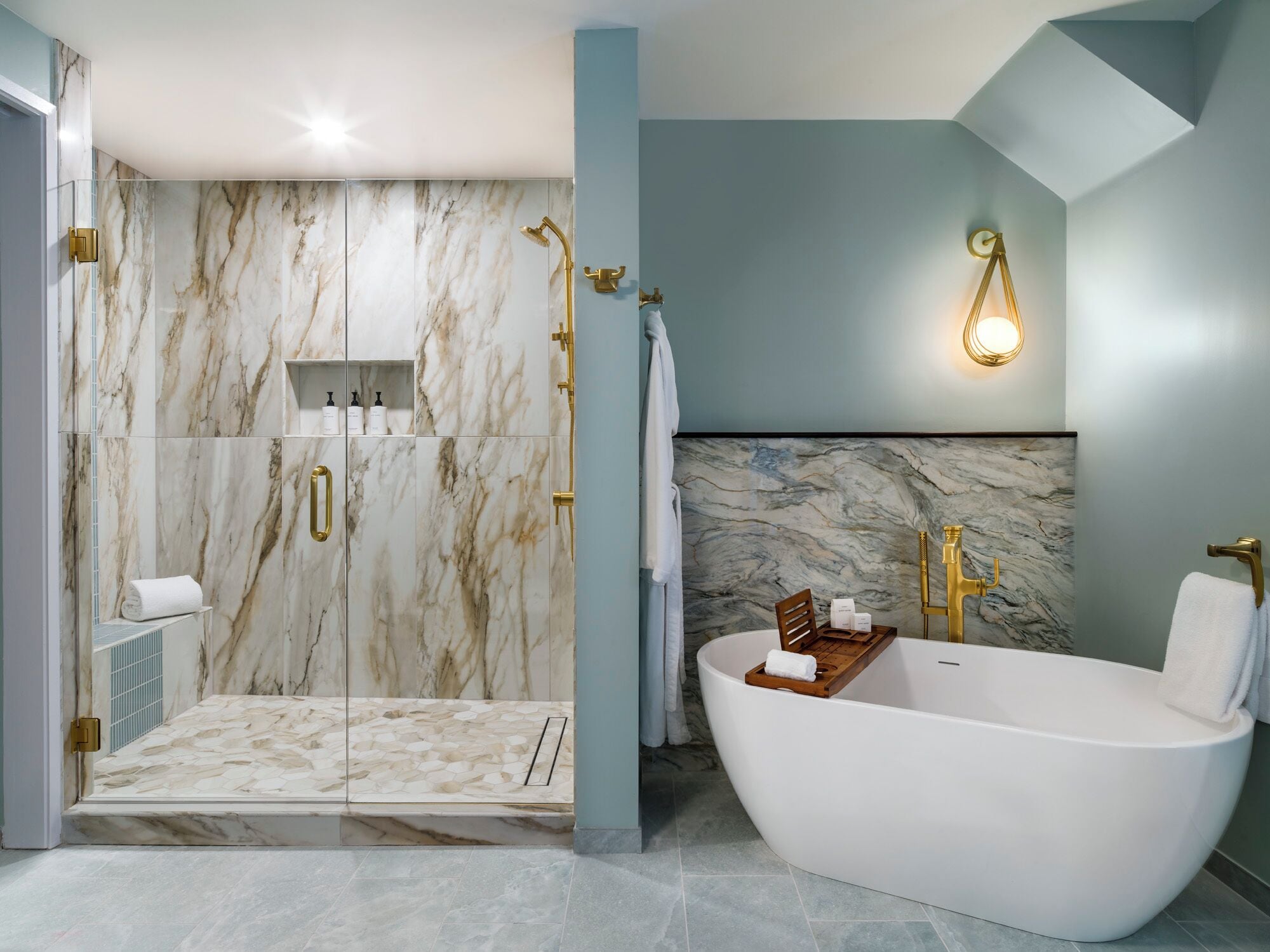 Une salle de bain moderne avec une baignoire sur pieds, une douche à parois de verre, des murs en marbre et des accessoires dorés.