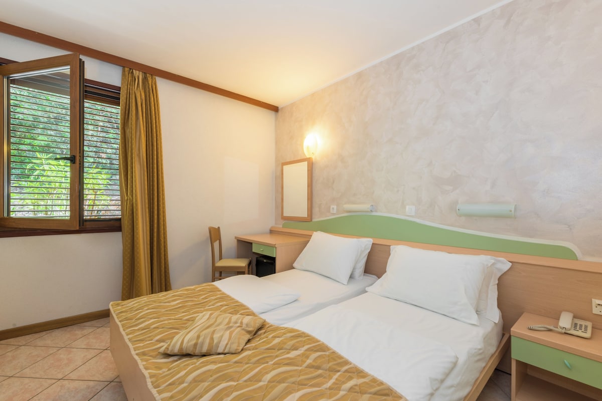 A hotel room with a bed, a desk, a chair, a telephone, and a window with curtains.