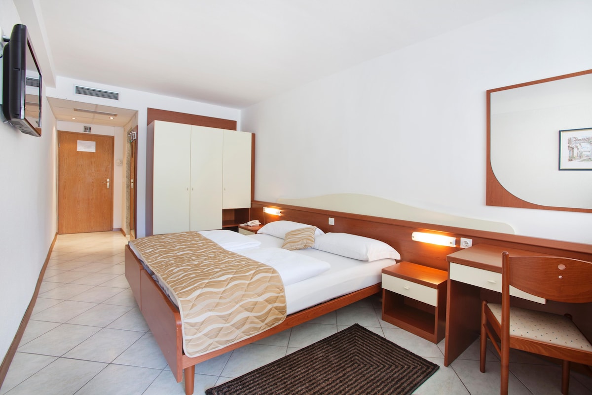A hotel room with a bed, bedside table, desk, chair, wardrobe, and a television.