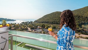 Varanda com vista desobstruída da paisagem costeira, uma tigela de frutas e um copo de suco de laranja.