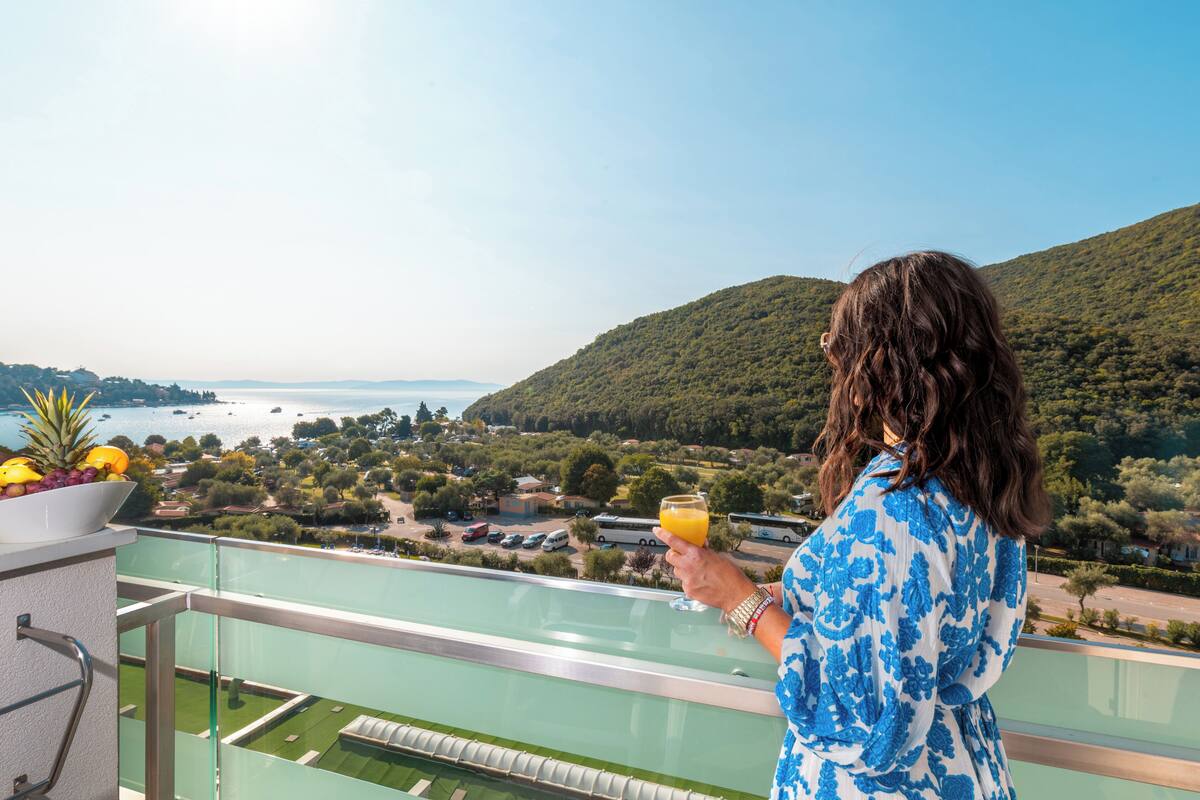 A balcony with a clear view of a coastal landscape, a bowl of fruit, and a glass of orange juice.