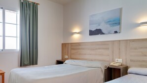Habitación de hotel con dos camas, cabecero de madera, mesita de noche con teléfono, lámpara de pared y ventana con cortinas.