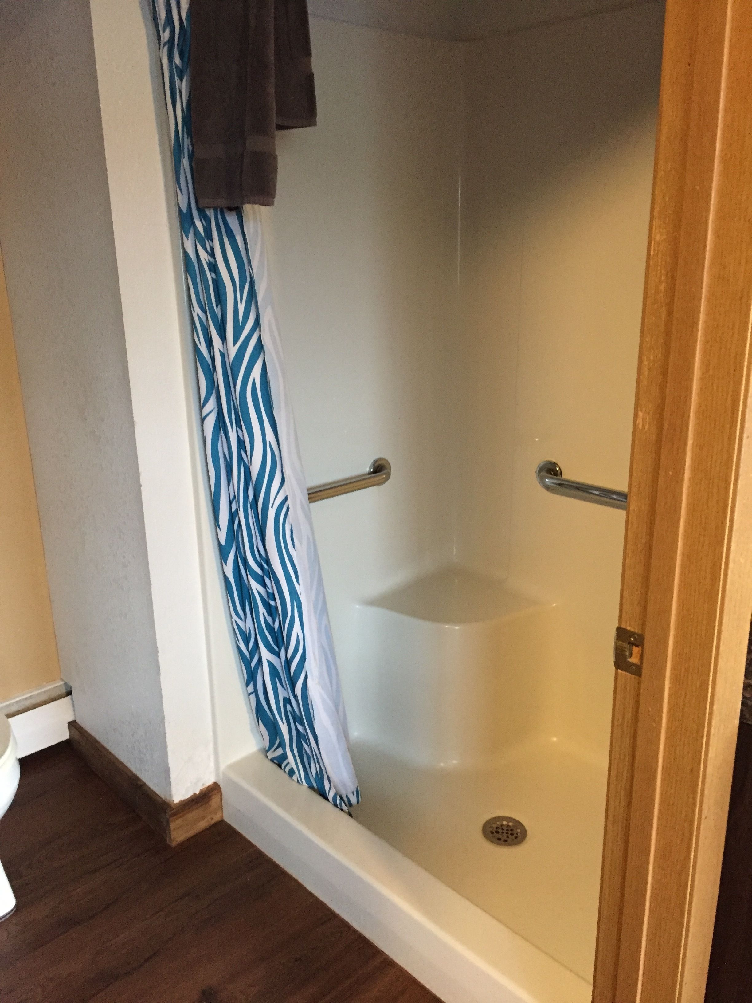 Eine barrierefreie Dusche mit Badewanne in Weiß, einem blauen und weißen Duschvorhang und einem Holzrahmen.