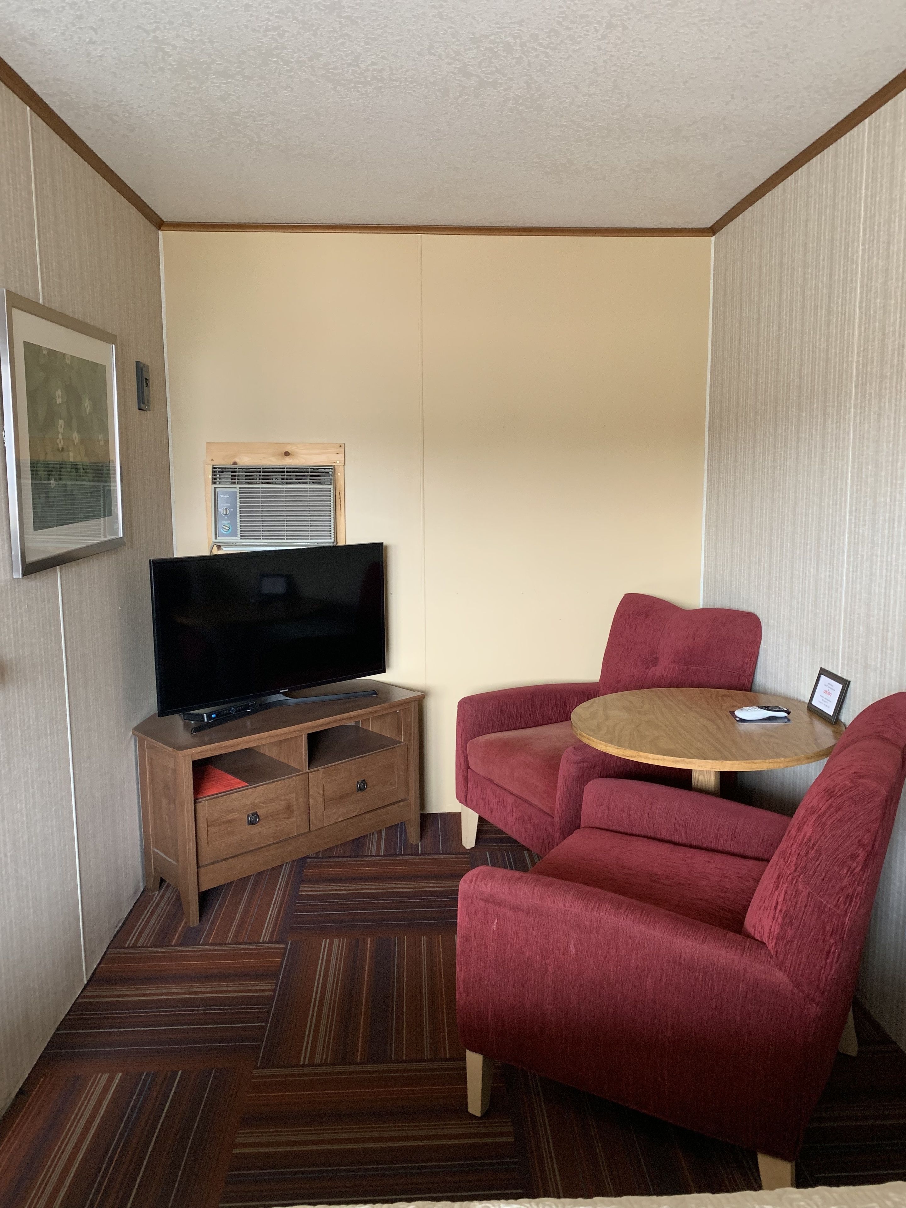 A compact living space with a flat-screen TV on a wooden stand, a red sofa, and a small wooden table.