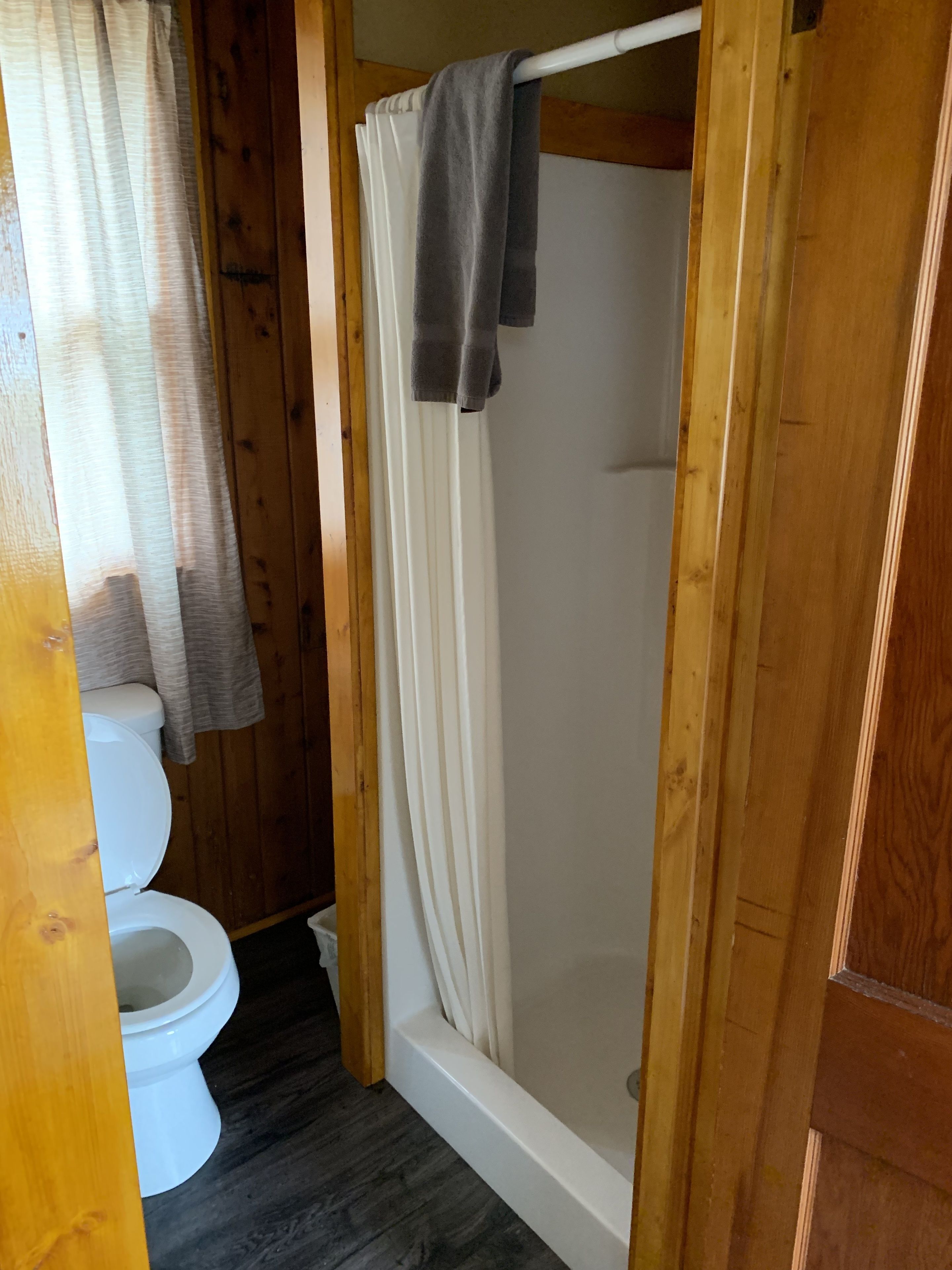 Ein Badezimmer aus Holz mit Toilette, einer Duschkabine mit Vorhang und Holzboden.