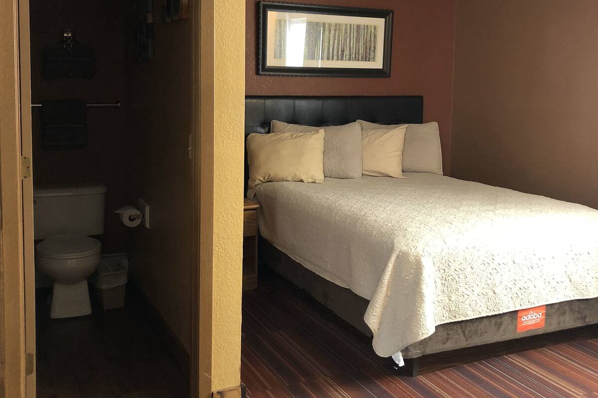 Une chambre d’hôtel avec un lit, une tête de lit, un tableau encadré au mur et un plancher en bois.