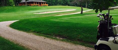 Um campo de golfe com um clube, um caminho de cascalho e um carrinho de golfe.