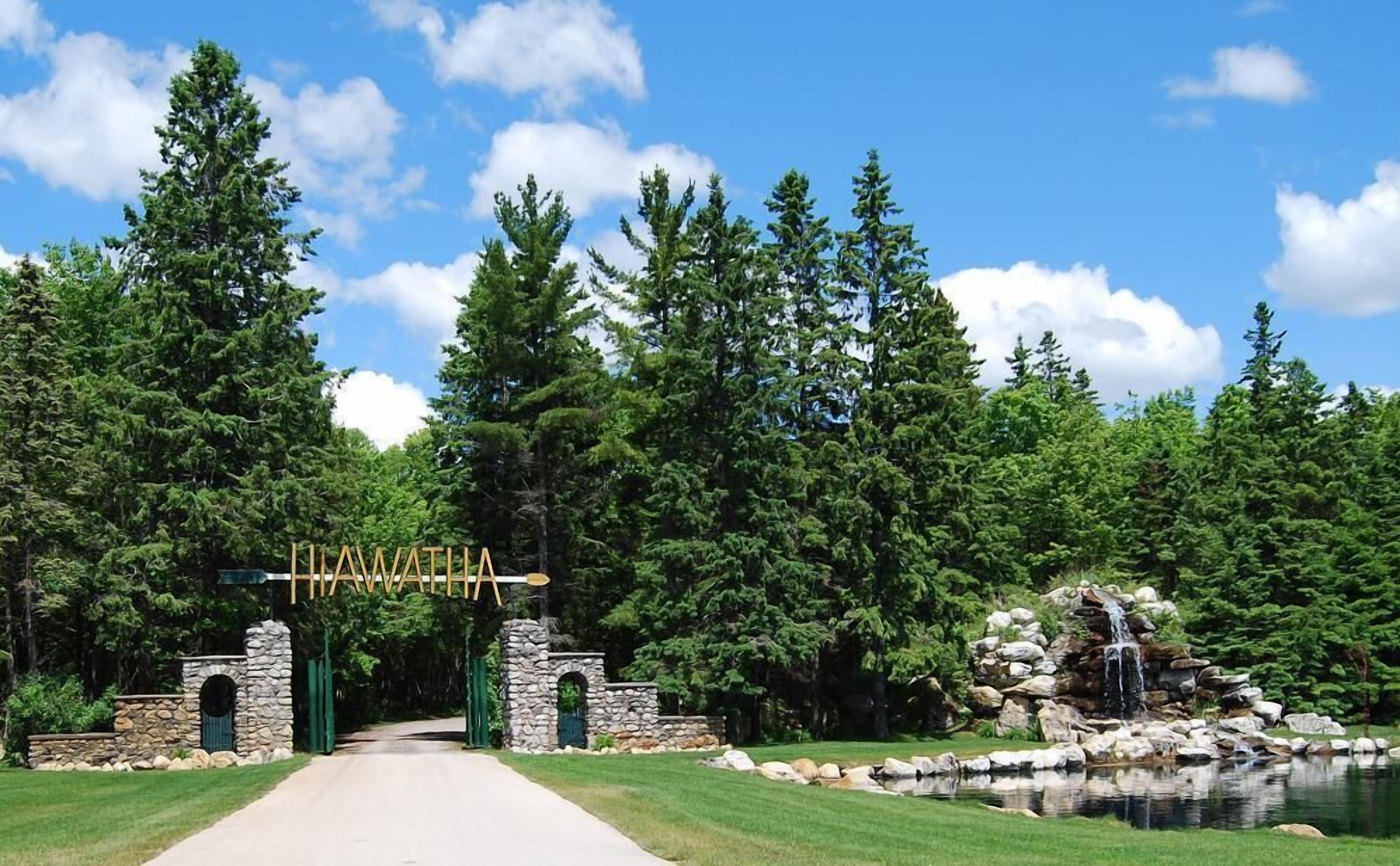 Un sentier mène à une arche en pierre sur laquelle est inscrit le nom « Hawatia », le tout étant entouré d’une végétation luxuriante et d’une petite cascade.