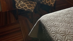 Een kamer met een houten vloer, een ronde tafel, twee gestreept beklede stoelen en een bed met een geborduurde spreideken.