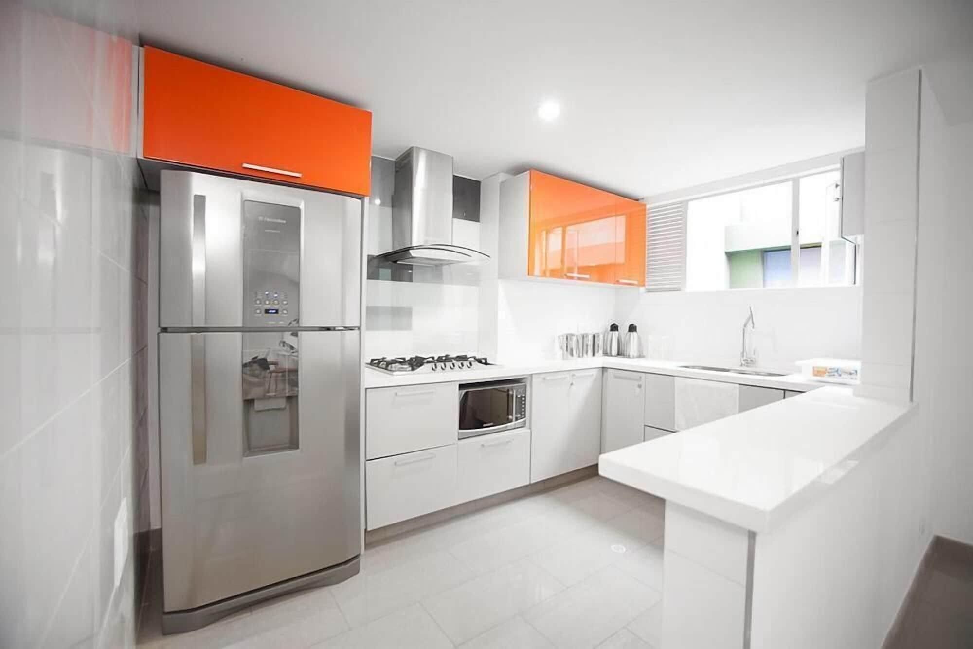 Una cocina moderna con electrodomésticos de acero inoxidable, armarios blancos y detalles en naranja.