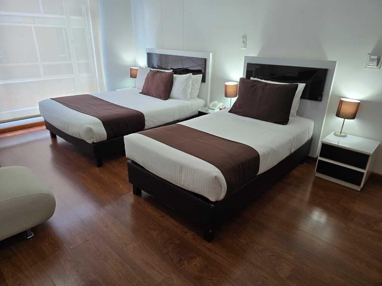 Habitación de hotel con dos camas, una mesita de noche con lámpara y una silla.