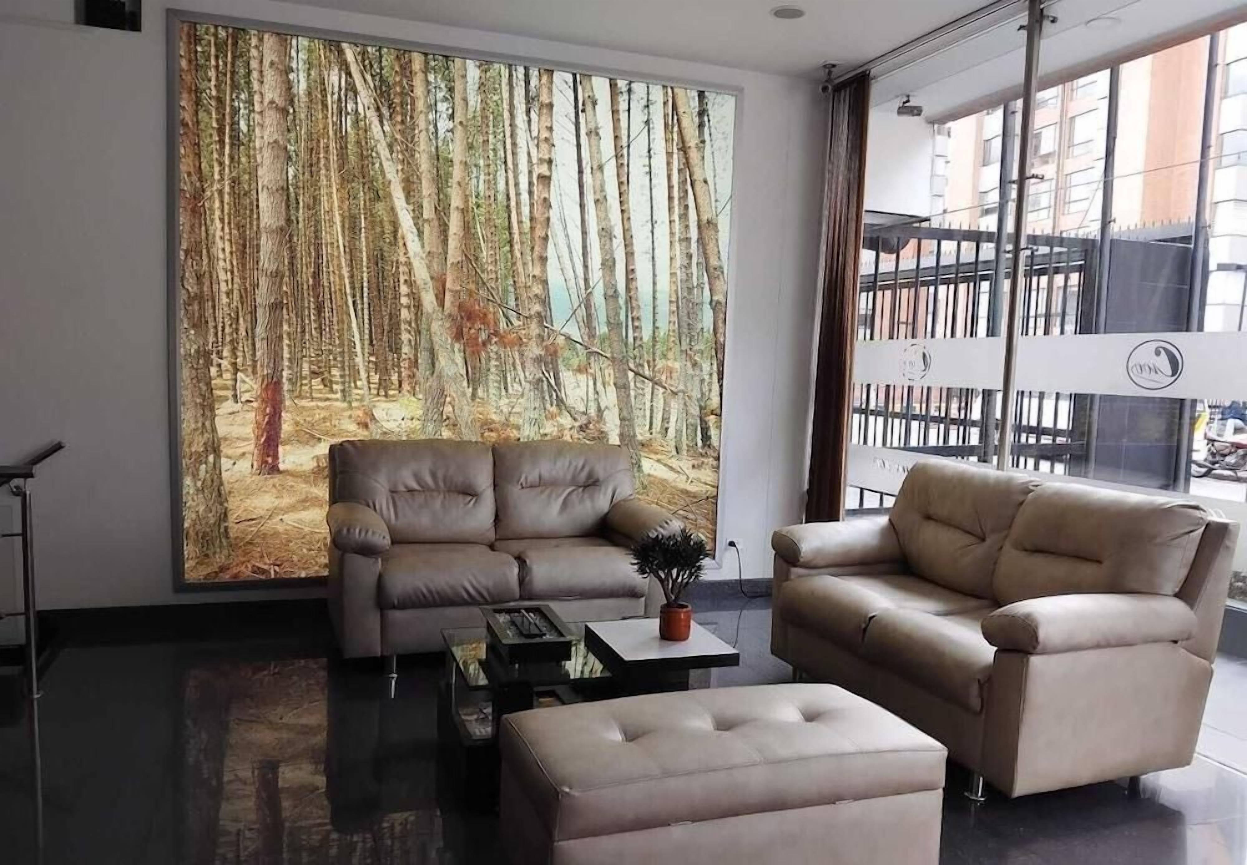 Un salón moderno con una gran obra de arte con temática de bosque, dos sofás color beige, una mesa de centro y vistas a la ciudad a través de amplios ventanales.