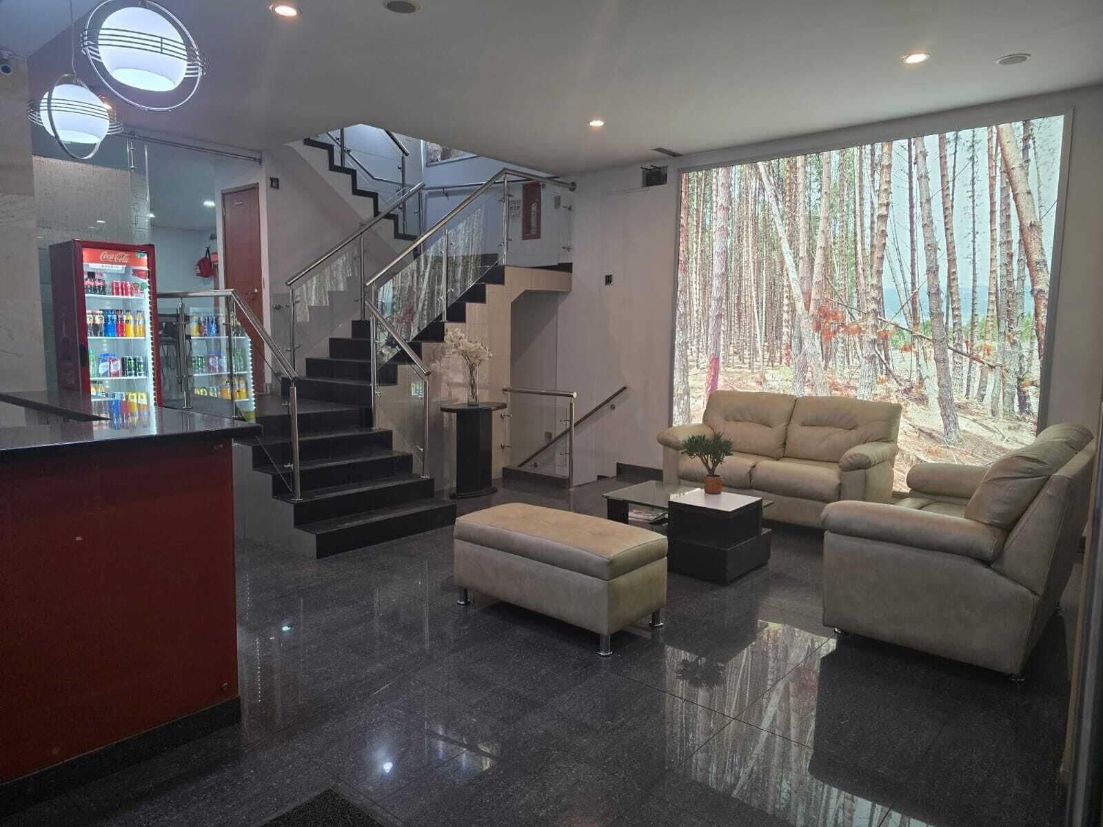 Una sala de estar moderna con sofá, reposapiés, mesa de centro y una escalera con barandillas de vidrio.
