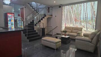 Una sala de estar moderna con sofá, reposapiés, mesa de centro y una escalera con barandillas de vidrio.