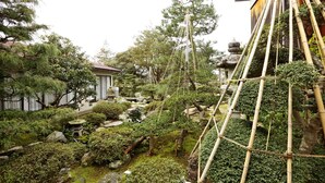 A traditional Japanese garden with rock formations, bamboo structures, and a small building. - Katsuzakikan (Tsubata)