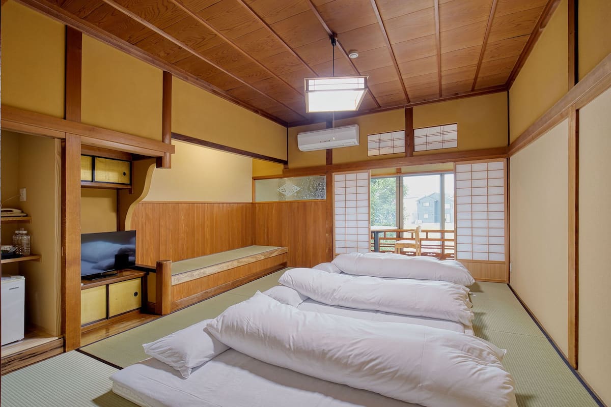 A traditional Japanese-style room with tatami flooring, a low wooden bed, a television, and a sliding door leading to an outdoor area.