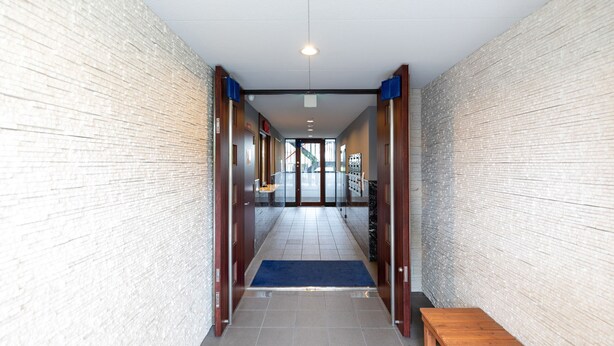 A hallway with a blue carpet leading to a door, wooden benches along the sides, and a tiled floor. - Tabist Gloire Osaka (Osaka)