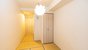 A hallway with a wooden door, a ceiling light fixture, and a wall clock. - Tabist Gloire Osaka (Osaka)