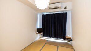 A room with tatami flooring, a ceiling fan, a mounted air conditioner, a television on a stand, and a window with dark curtains. - Tabist Gloire Osaka (Osaka)