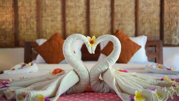 Cama com cabeceira trançada, almofadas brancas e arranjo de toalhas decorativo em formato de cisnes com flores.