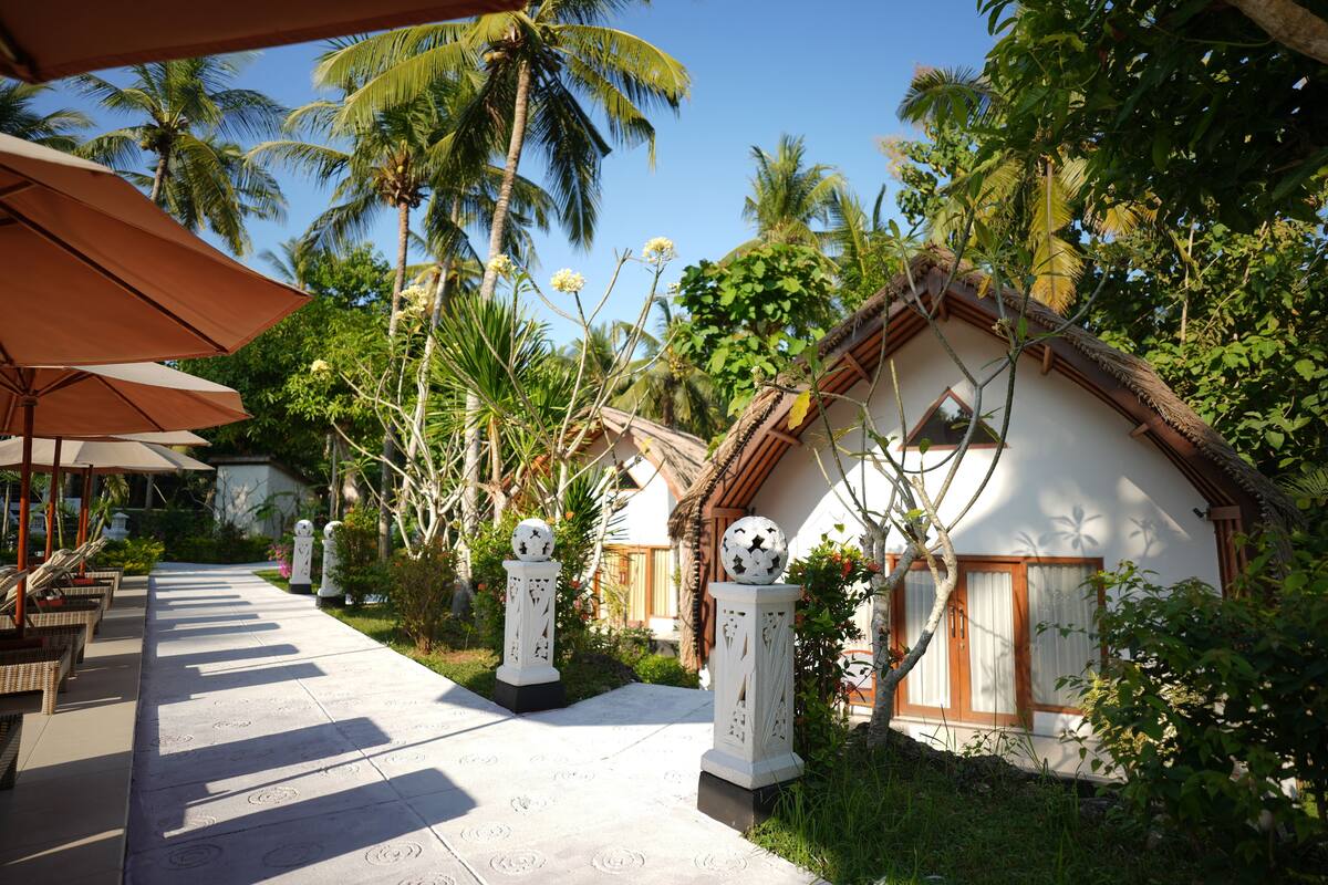 A pathway leading to a building with a thatched roof, surrounded by palm trees and greenery.