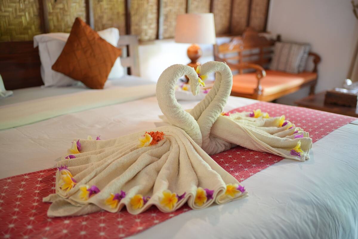 A neatly made bed with a decorative swan towel arrangement and a red patterned bedspread.
