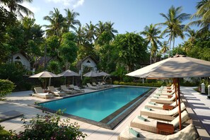 A swimming pool with lounge chairs and umbrellas, surrounded by palm trees and a tropical garden. - Coco Resort Penida (Penida Island)