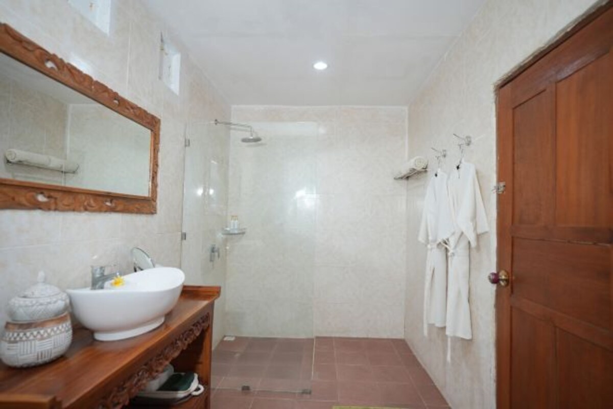 A bathroom with a large mirror, a white sink, a shower, and a wooden door.