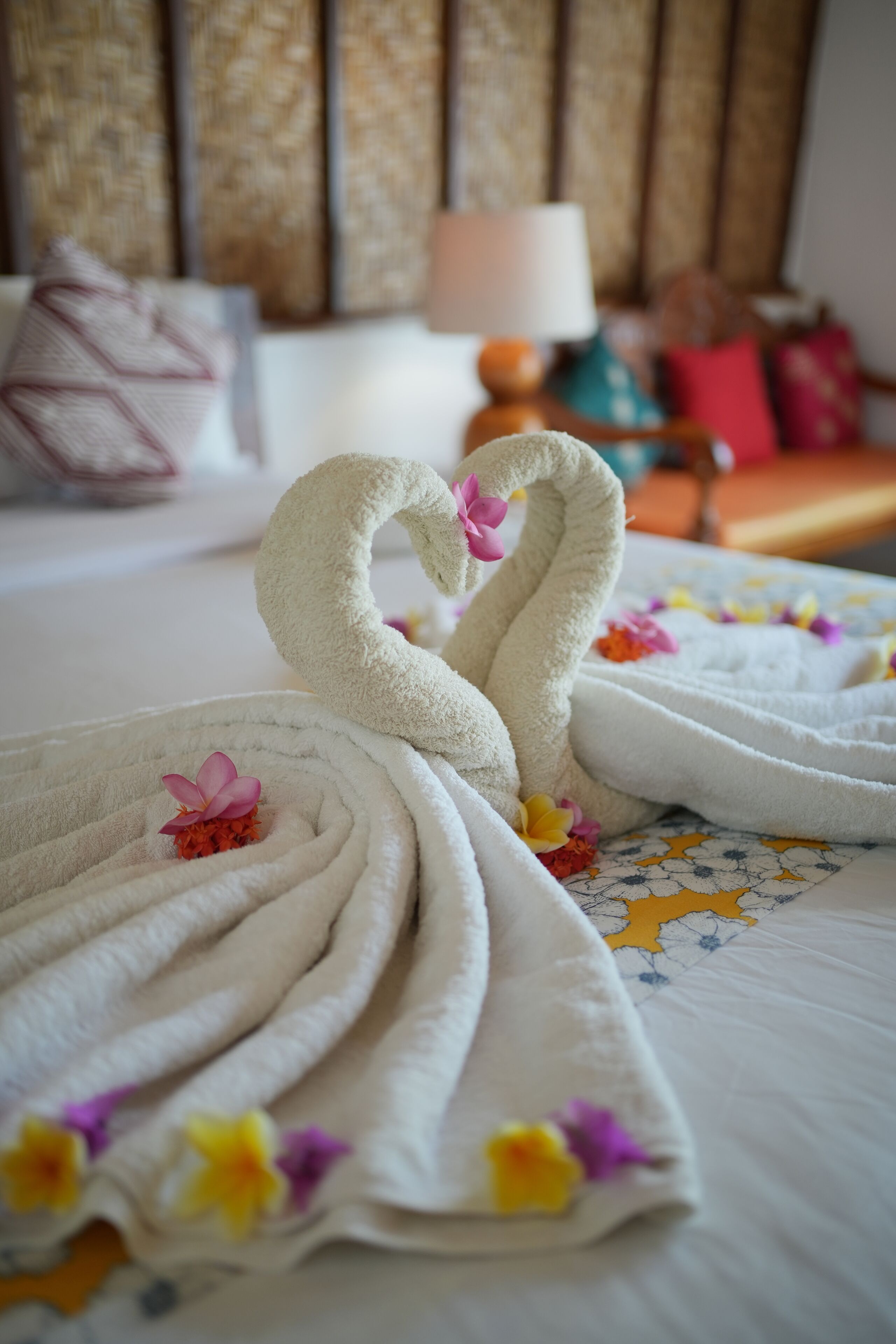 A neatly made bed with two towels arranged in a heart shape, adorned with flowers.