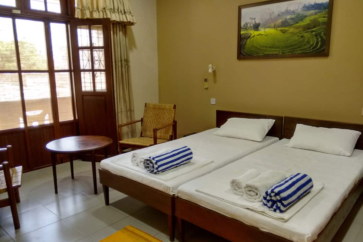 A hotel room with two beds, a chair, a small table, and a painting on the wall.