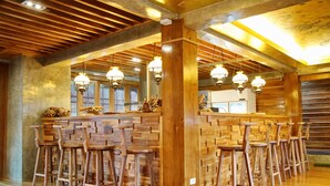 Un espace bar avec des tabourets de bar en bois et un plafond haut avec des poutres apparentes.