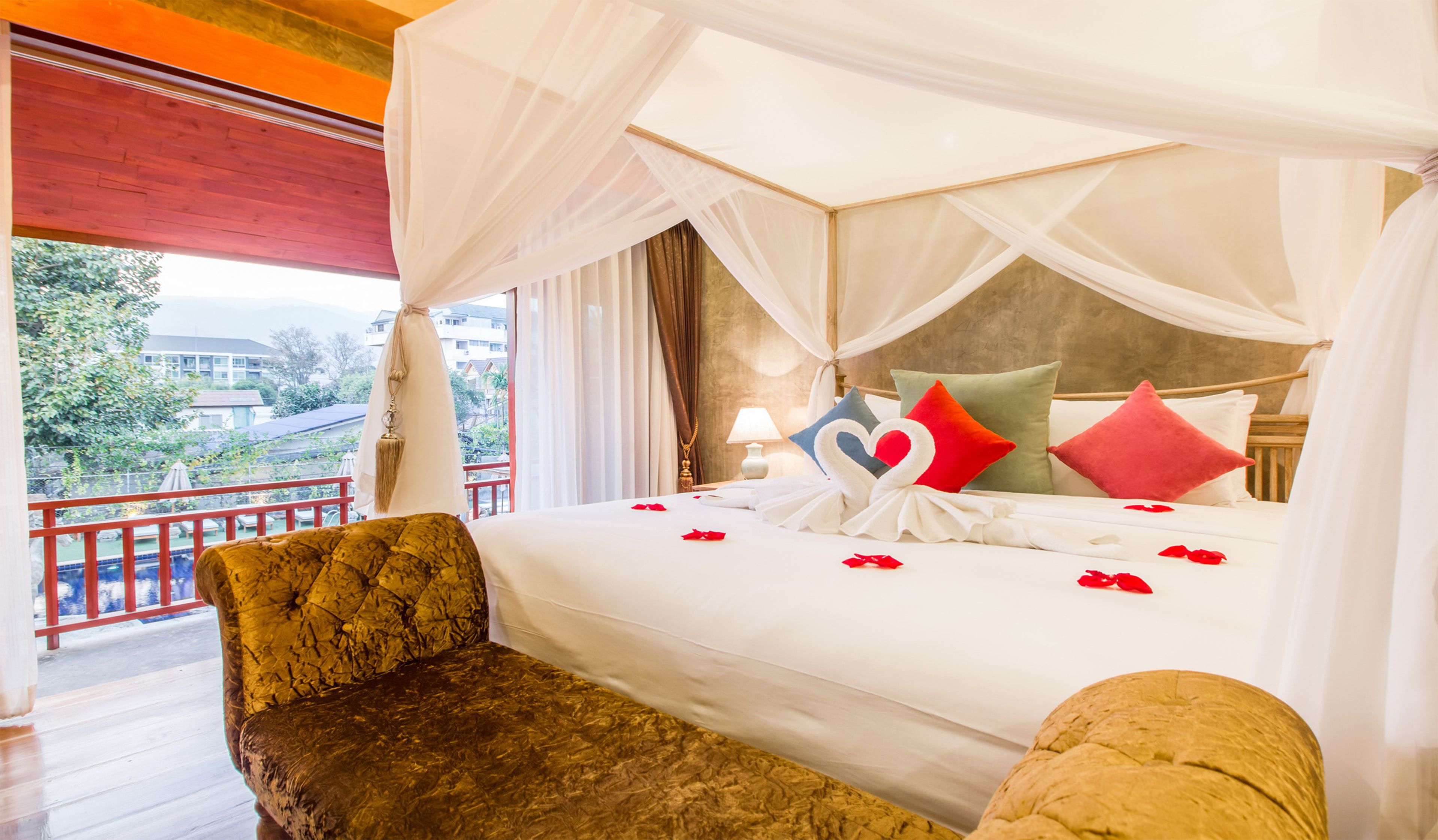 A four-poster canopy bed with a view of a pool and buildings outside.