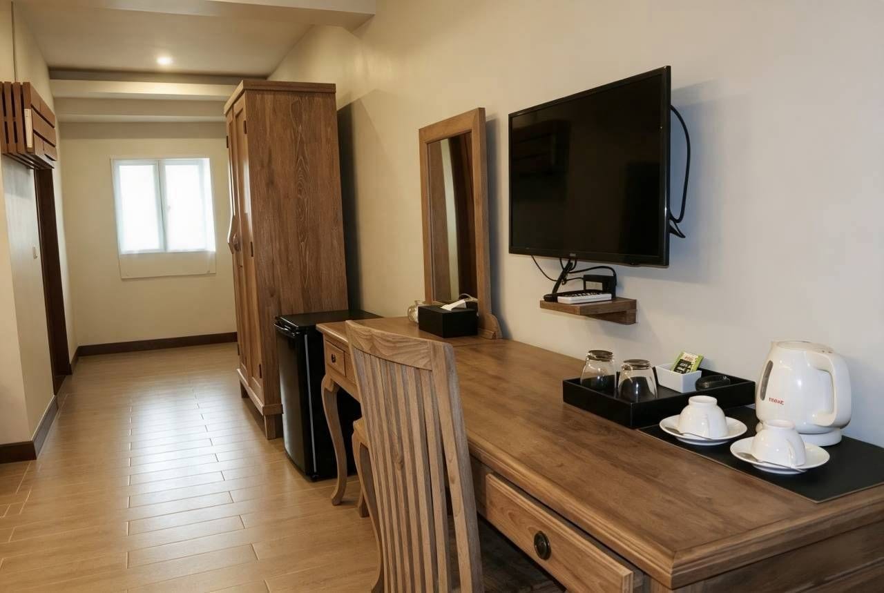 A hotel room with a wooden desk, a flat-screen TV, a mirror, and a coffee maker.