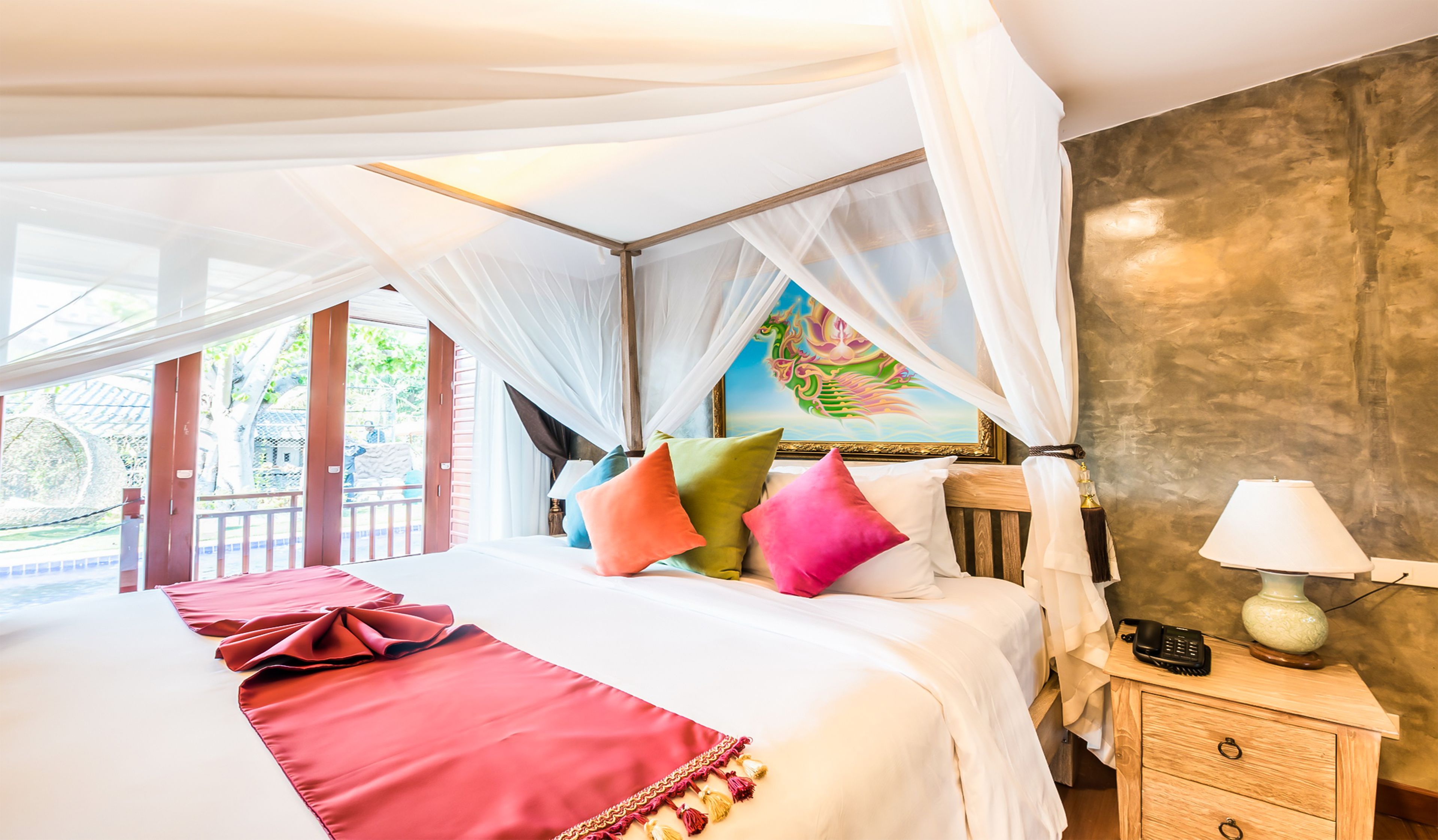 A bedroom with a bed, colorful pillows, a bedside table with a lamp, and a painting on the wall.